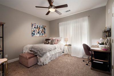 Carpeted bedroom with bed, ceiling fan, and desk